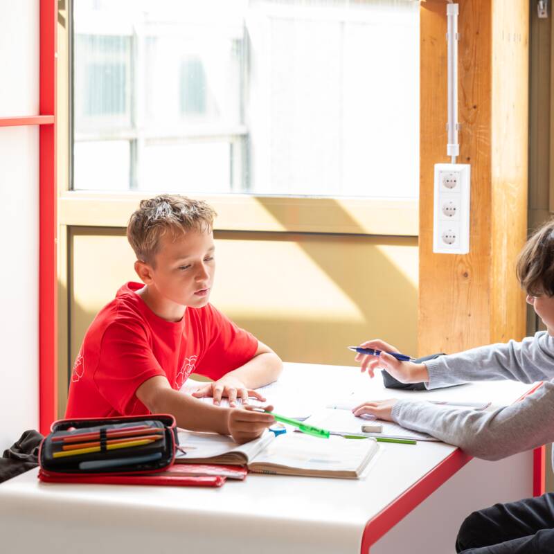 Zwei Schüler sitzen an einem Tisch in einer Lerninsel und arbeiten zusammen an Aufgabenheften.