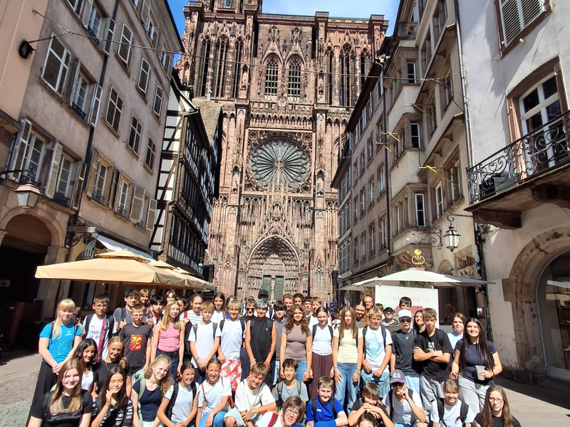 Eine große Schülergruppe posiert mit ihren Lehrerinnen vor dem Straßburger Münster.
